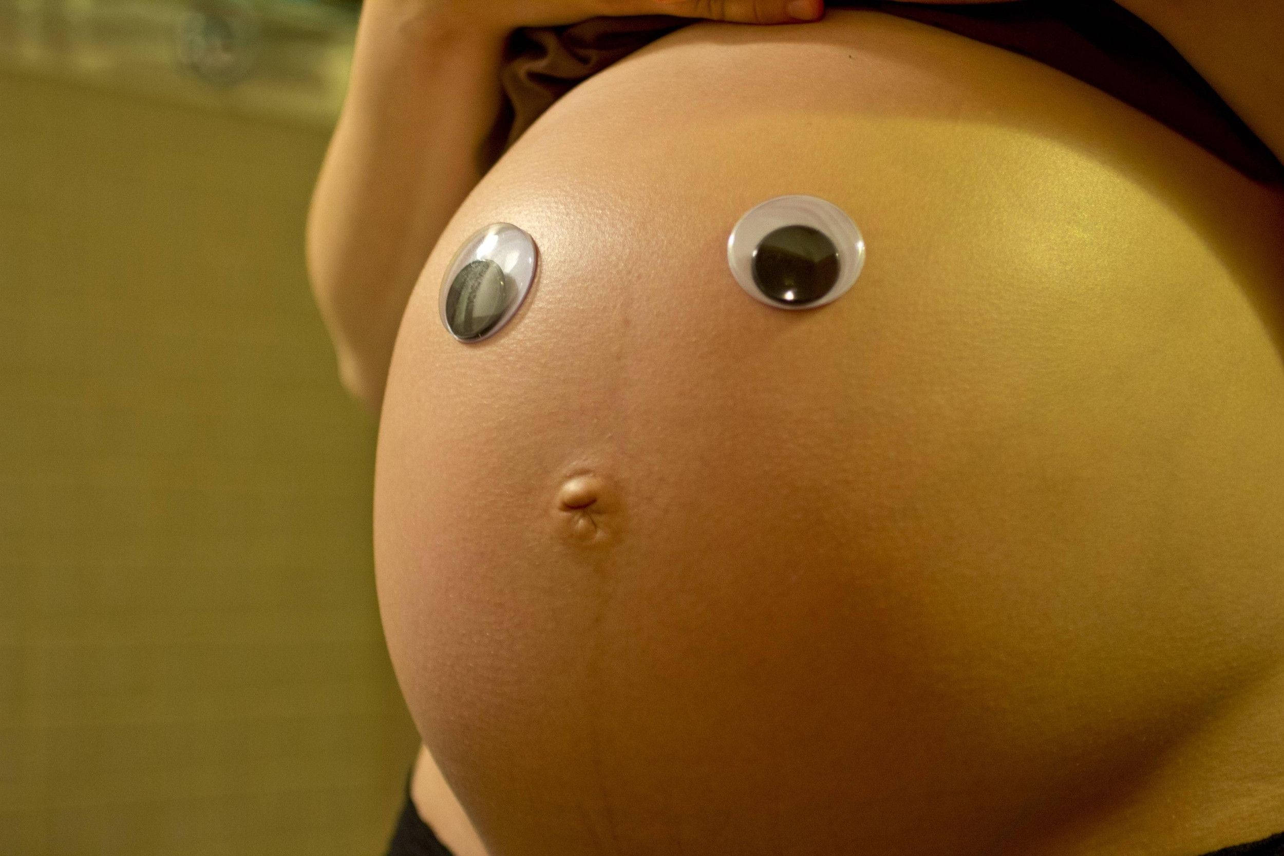 Pregnant 桌布 壁紙 — 一個大肚腩的特寫，上面裝飾著凸眼，營造出俏皮的嬰兒臉表情。