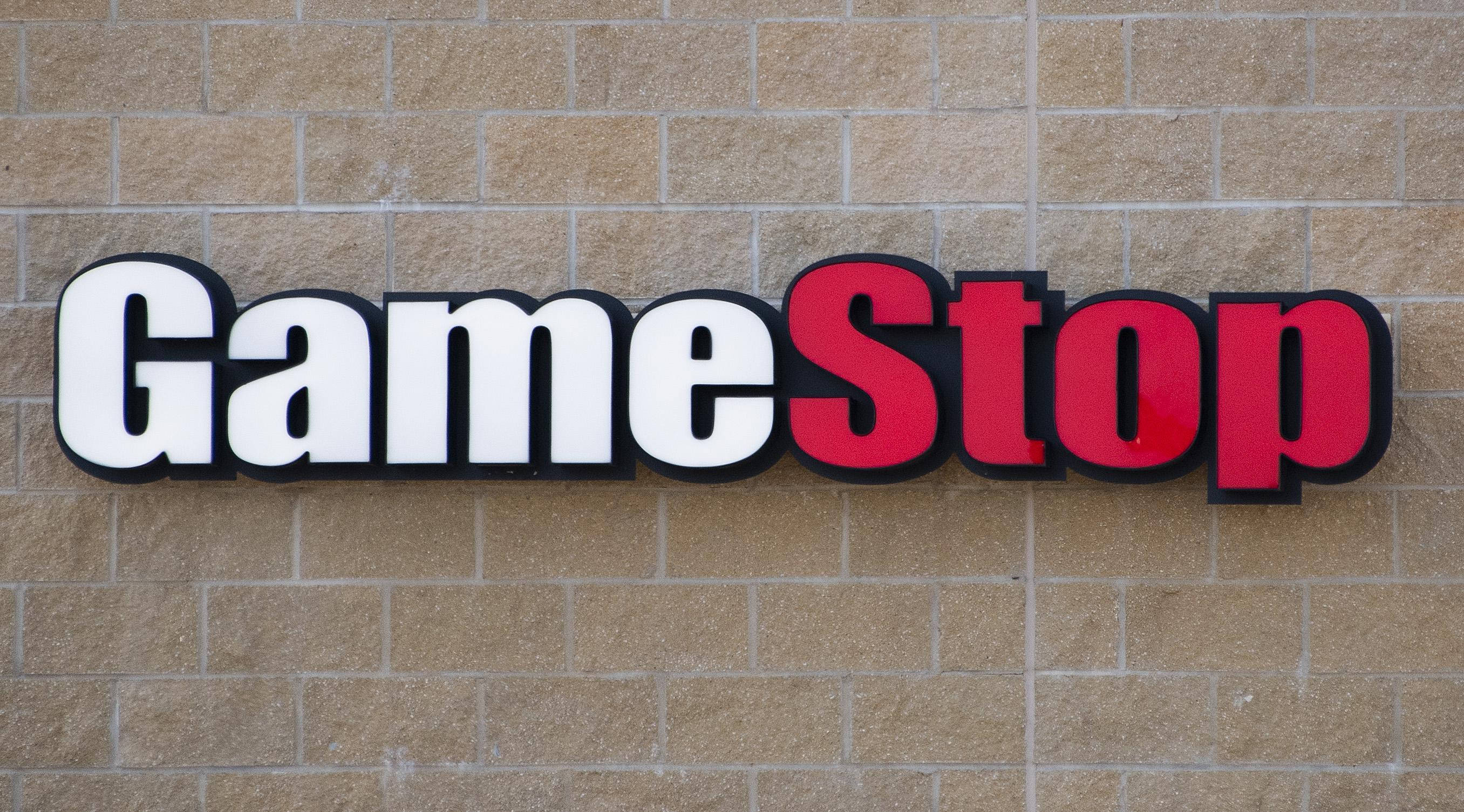 GameStop 桌布 壁紙 — 一個大膽的GameStop標誌，白色和紅色字母安裝在米色磚牆上。