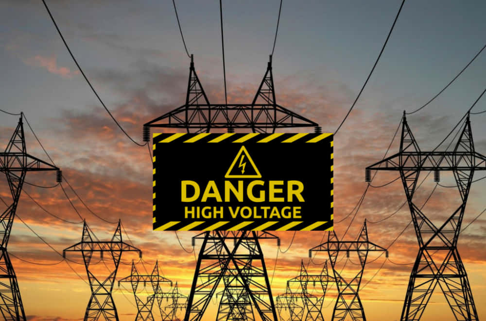 Power Lines 桌布 壁紙 — 一個大膽的危險標誌警告高電壓，背景是戲劇性的日落天空，襯托著高聳的輸電線結構。