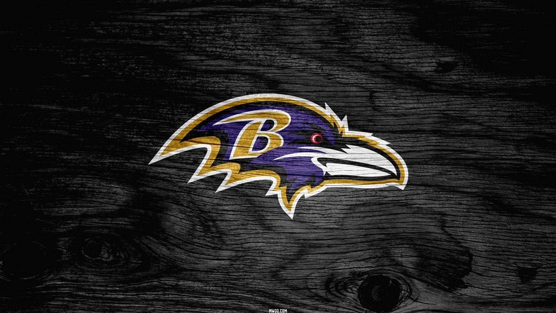 Ravens 桌布 壁紙 — 一個大膽的巴爾的摩烏鴉隊標誌，以紫色、金色和黑色為主色，在深色紋理木質背景上格外突出。