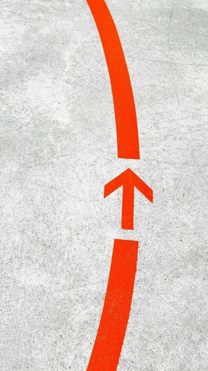  壁紙 — 一個大膽的橙色箭頭畫在紋理混凝土上，沿著彎曲路徑指向上方。