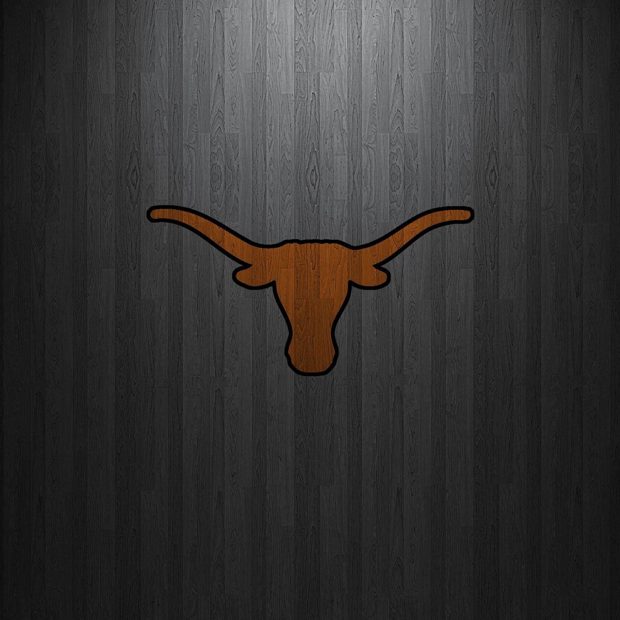 Texas Longhorn 桌布 壁紙 — 一個大膽的橙色長角牛標誌，帶有黑色輪廓，居中在深灰色木紋背景上。