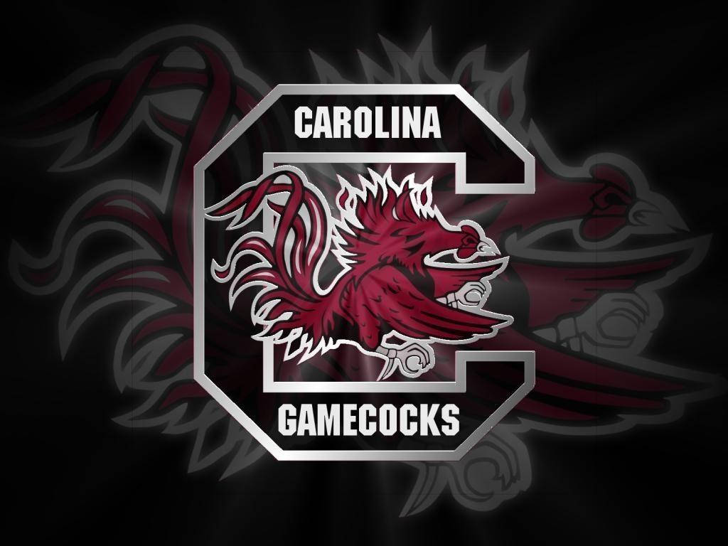 South Carolina Gamecocks 桌布 壁紙 — 一個大膽的深紅色鬥雞吉祥物標誌，位於銀色 'C' 中央，帶有 'CAROLINA' 和 'GAMECOCKS' 文字，背景為深色並帶有褪色羽毛圖案。