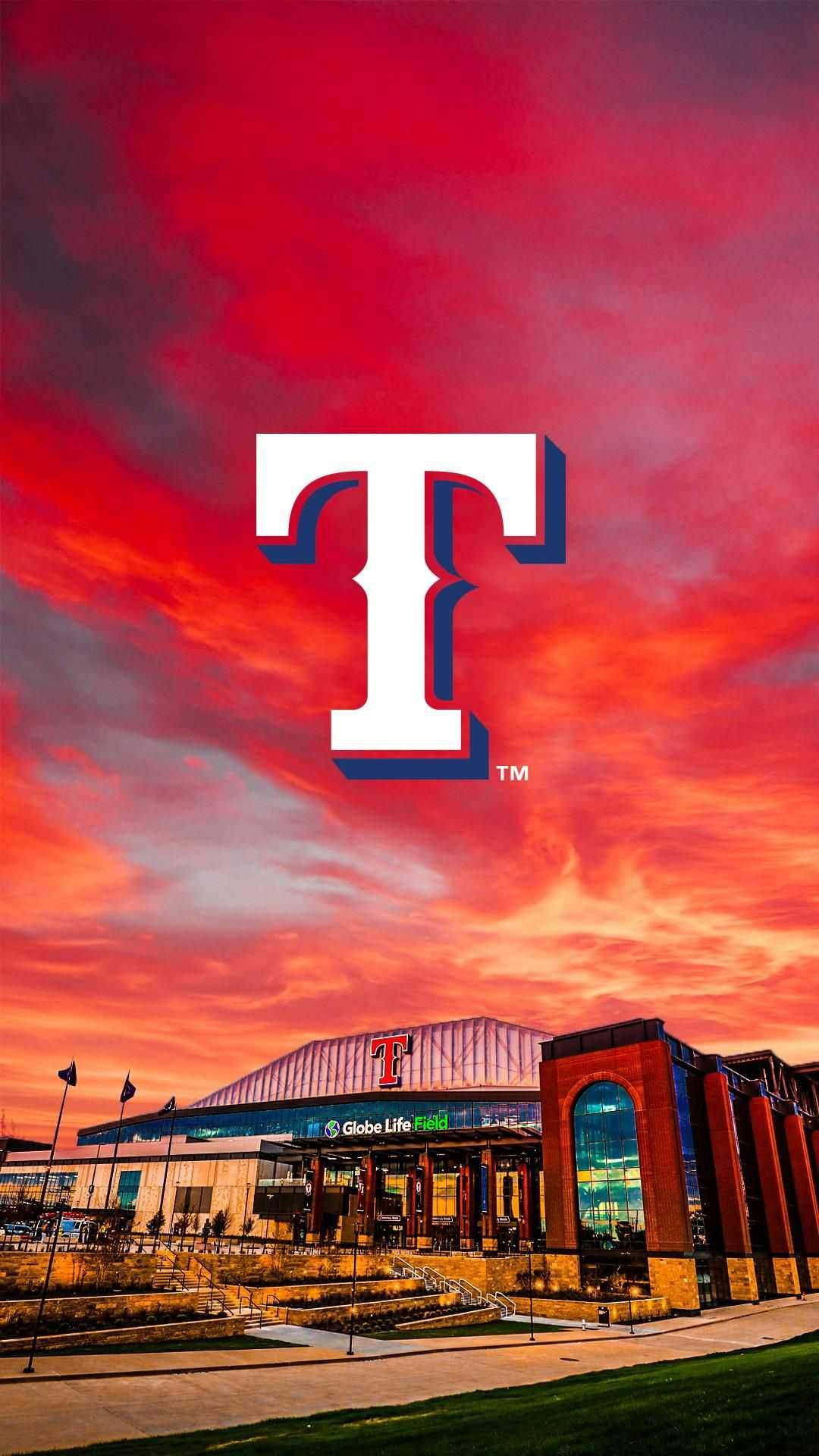 Texas Rangers 桌布 壁紙 — 一個大膽的白色德州遊騎兵隊 'T' 標誌，在環球人壽球場上空火紅橙色的夕陽天空中佔據主導地位。
