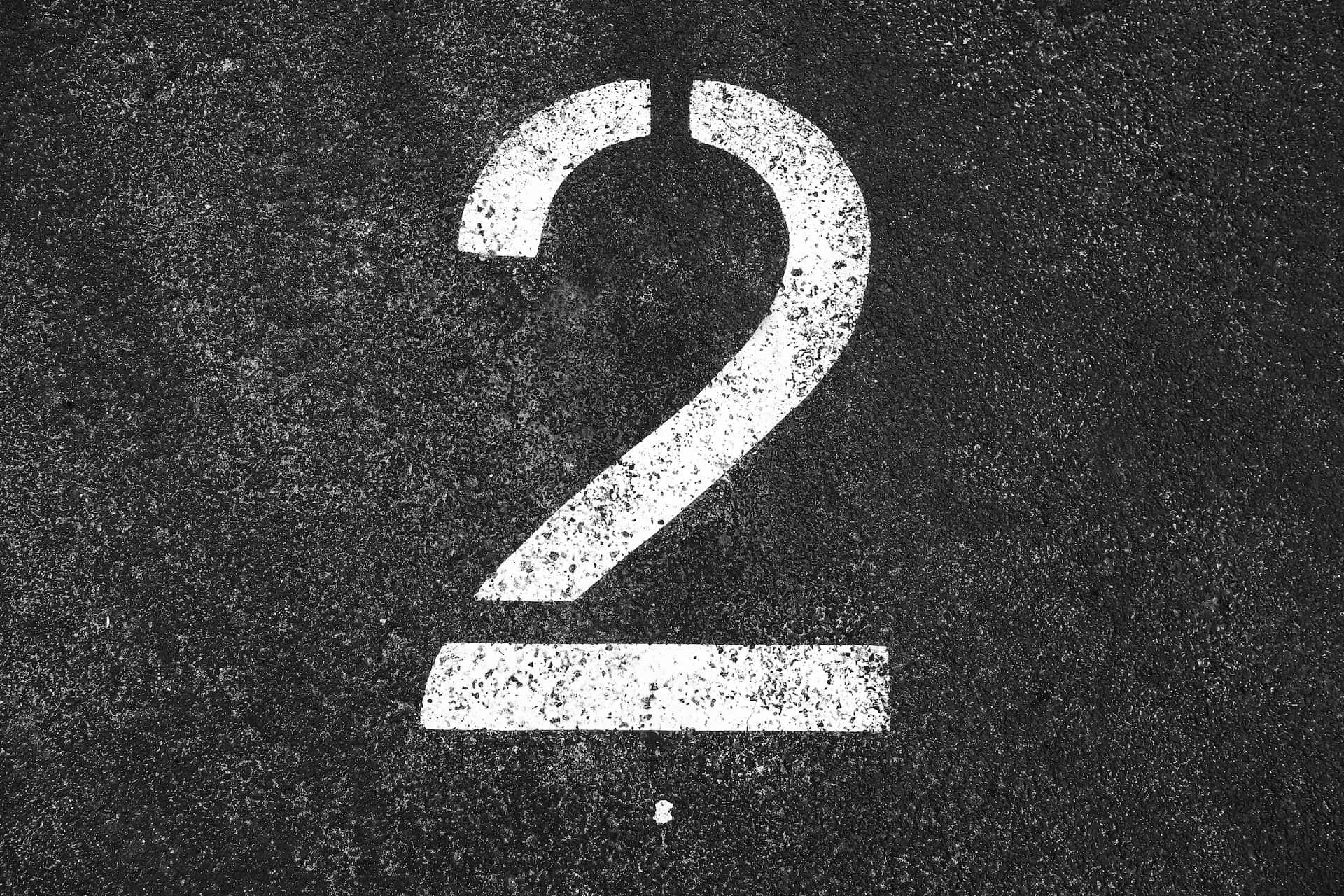 Number 桌布 壁紙 — 一個大膽的白色數字二，畫在粗糙的瀝青上，邊緣有缺損，質地有斑點。