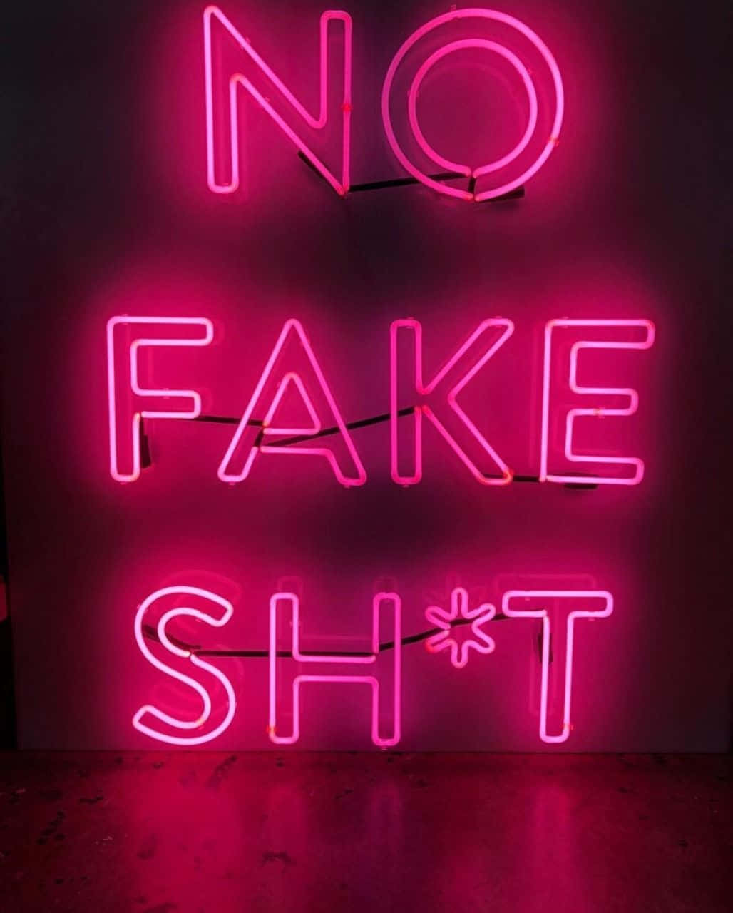 Neon Pink 桌布 壁紙 — 一個大膽的粉紅色霓虹燈牌寫著「NO FAKE SH*T」，在深色牆壁上投射出鮮豔的光芒到地板上。