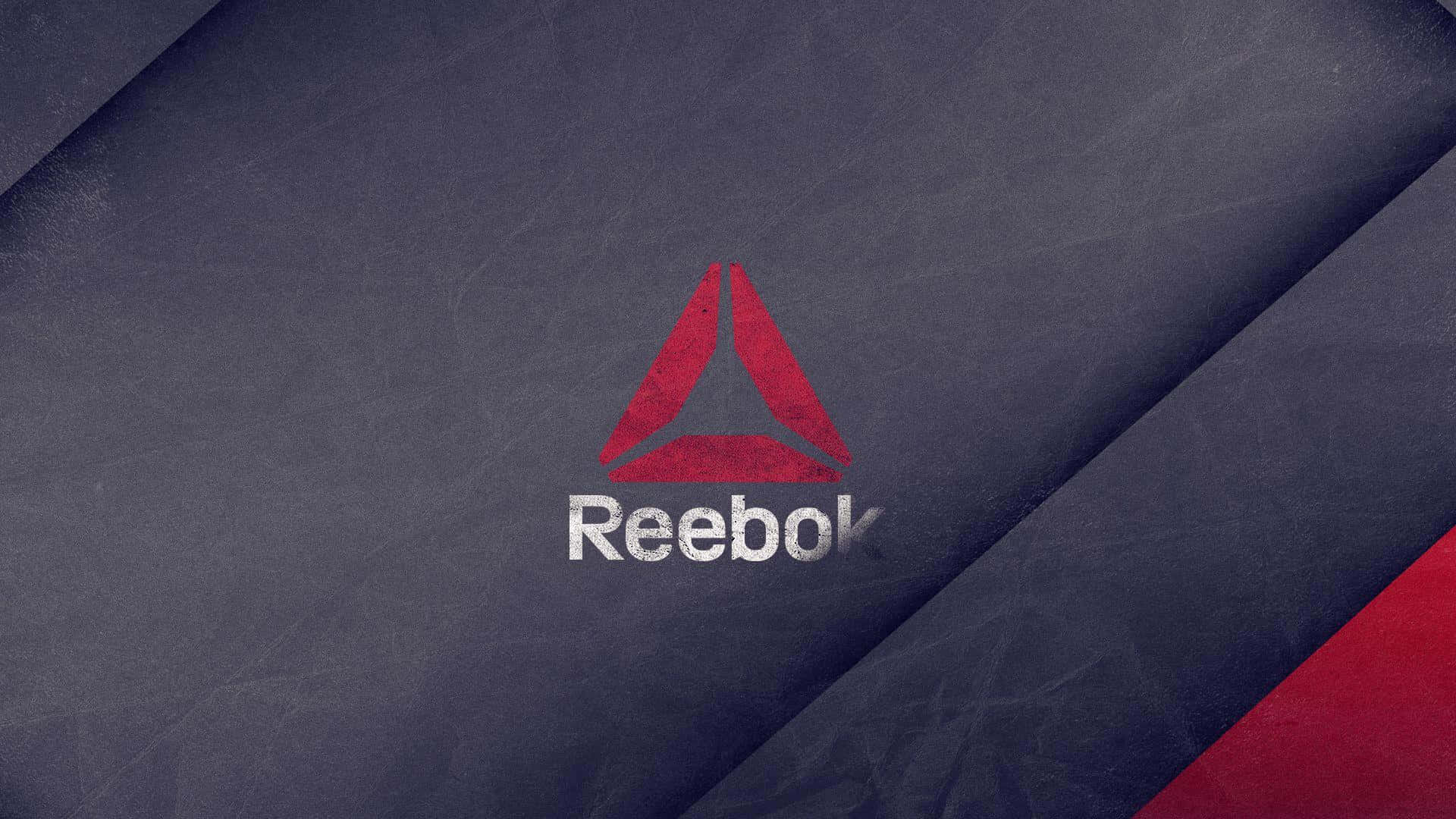 Reebok 桌布 壁紙 — 一個大膽的紅色 Reebok 標誌，白色文字居中，位於帶有紋理的深藍色布料背景上，並帶有紅色對角線裝飾。
