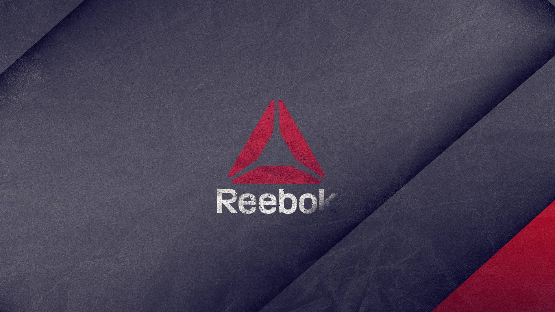 Reebok 桌布 壁紙 — 一個大膽的紅色 Reebok 標誌，帶有白色文字，位於有紋理的深藍色布料背景上，並帶有紅色對角線點綴。