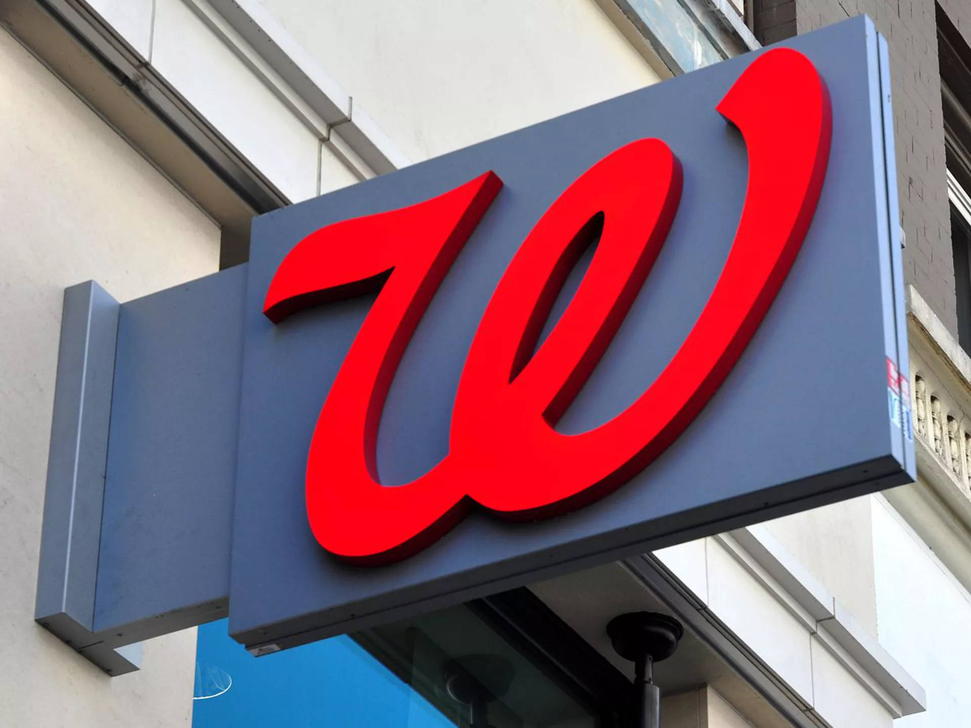 標誌 桌布 壁紙 — 一個大膽的紅色 Walgreens 'W' 標誌招牌安裝在灰色盒子上，背景是淺色建築物外牆。