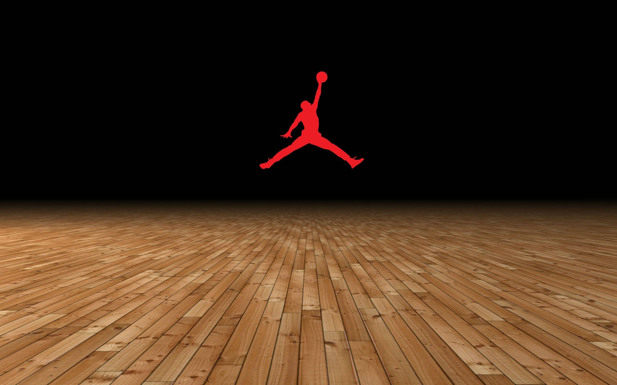 Jordan Logo 桌布 壁紙 — 一個大膽的紅色Jordan標誌漂浮在拋光木製籃球場上方，背景是漆黑的天空。