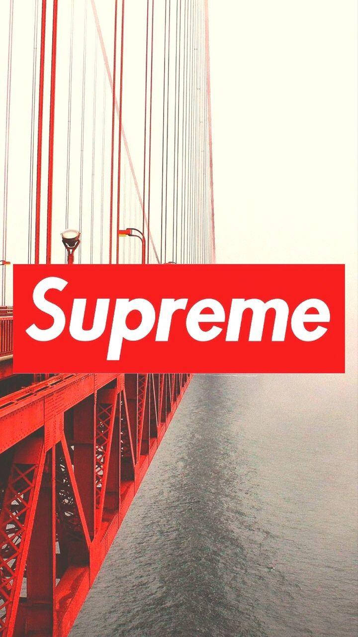 supreme 桌布 壁紙 — 一個大膽的紅色Supreme標誌疊加在金門大橋的鋼結構和寧靜水面的低角度視圖上。