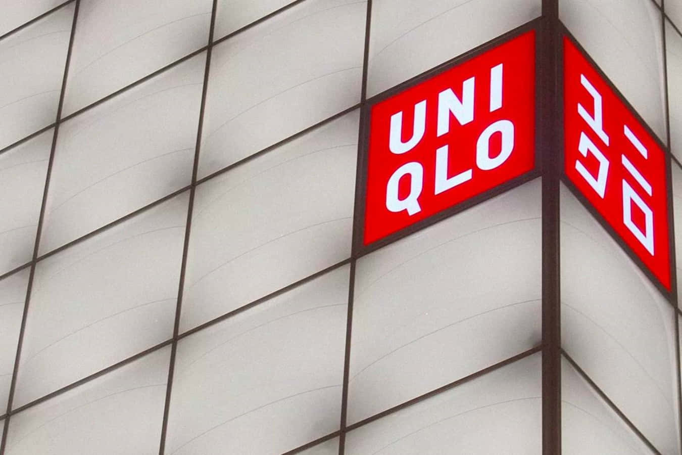 Uniqlo 桌布 壁紙 — 一個大膽的紅色Uniqlo標誌，帶有白色字體和韓文字，在現代建築的瓷磚外牆上發光。