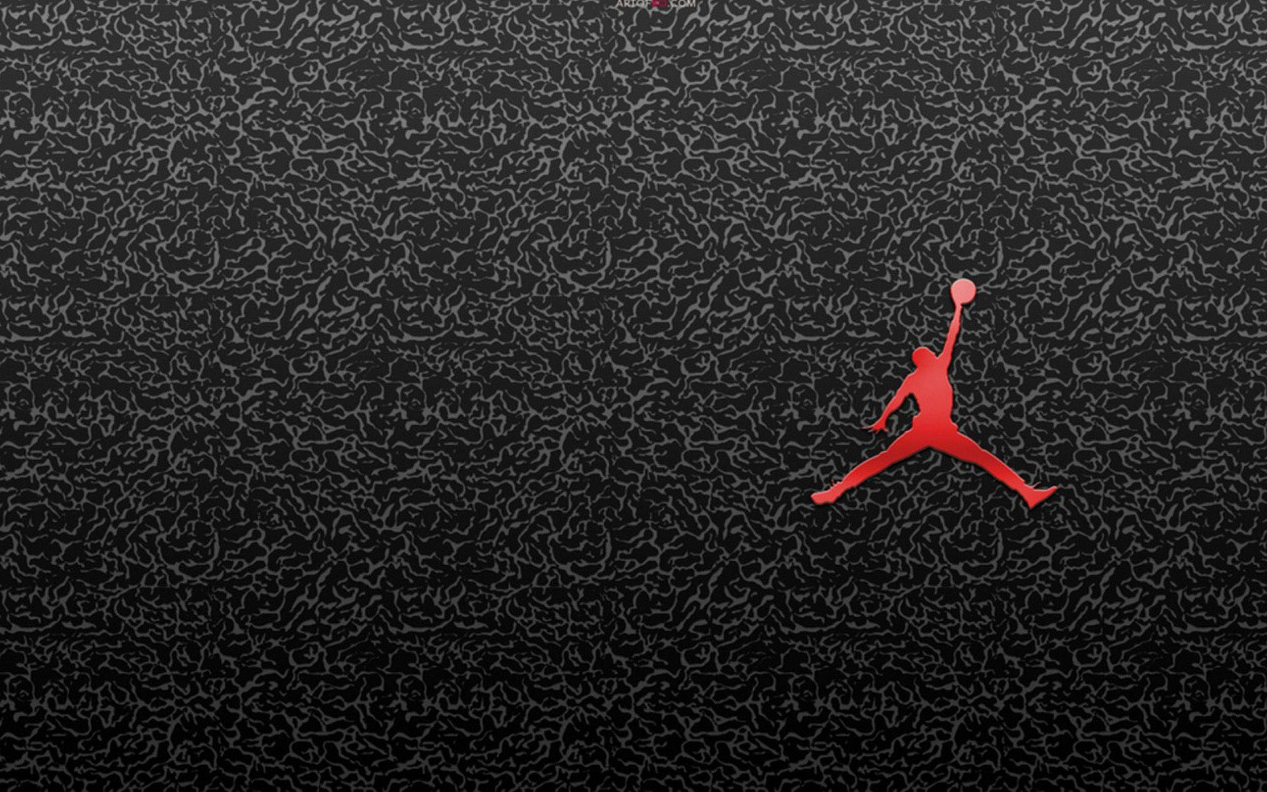 Jordan Logo 桌布 壁紙 — 一個大膽的紅色剪影，描繪一名籃球運動員在半空中持球，背景為帶紋理的黑色。