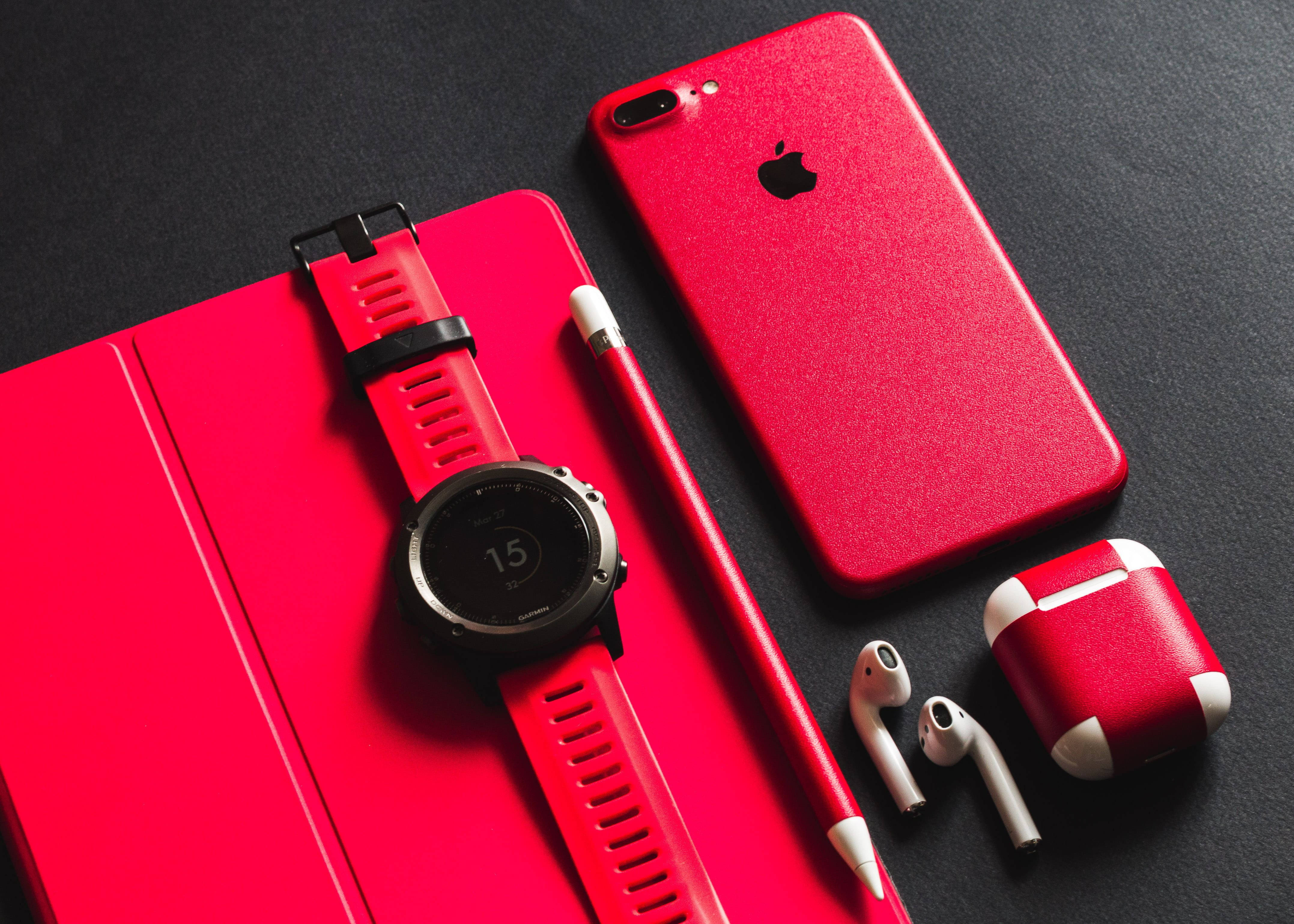 AirPods 桌布 壁紙 — 一個大膽的紅色科技設置，包括智慧手錶、電話、耳機和觸控筆，排列在深色表面上。