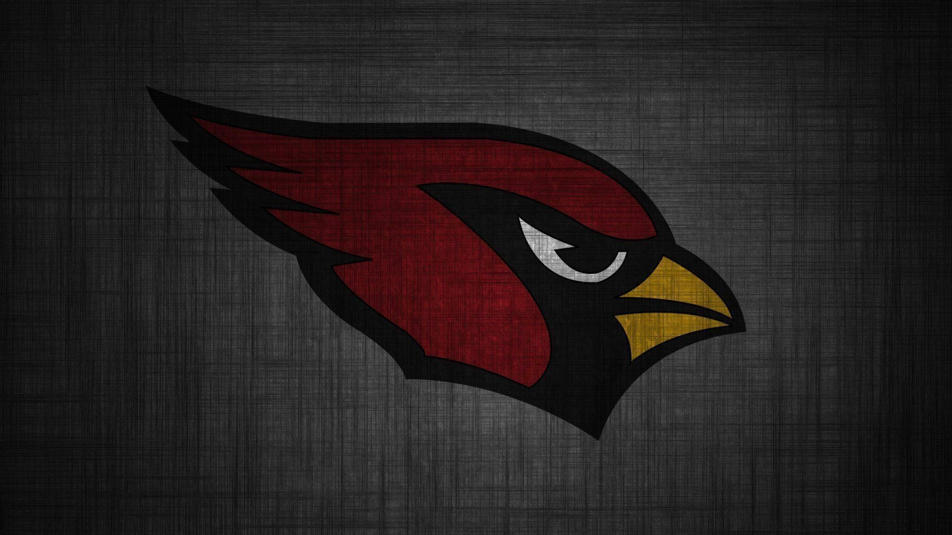 Cardinals 桌布 壁紙 — 一個大膽的紅色紅雀標誌，帶有黑色和黃色點綴，在深色紋理灰色背景上脫穎而出。