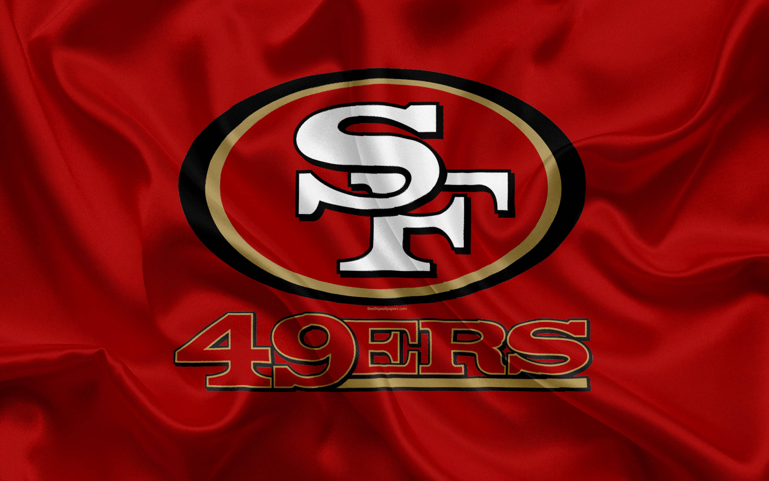 NFL Team Logo 桌布 壁紙 — 一個大膽的舊金山49人隊標誌在豐富的紅色緞面布料上閃耀，帶有戲劇性的褶皺和高光。