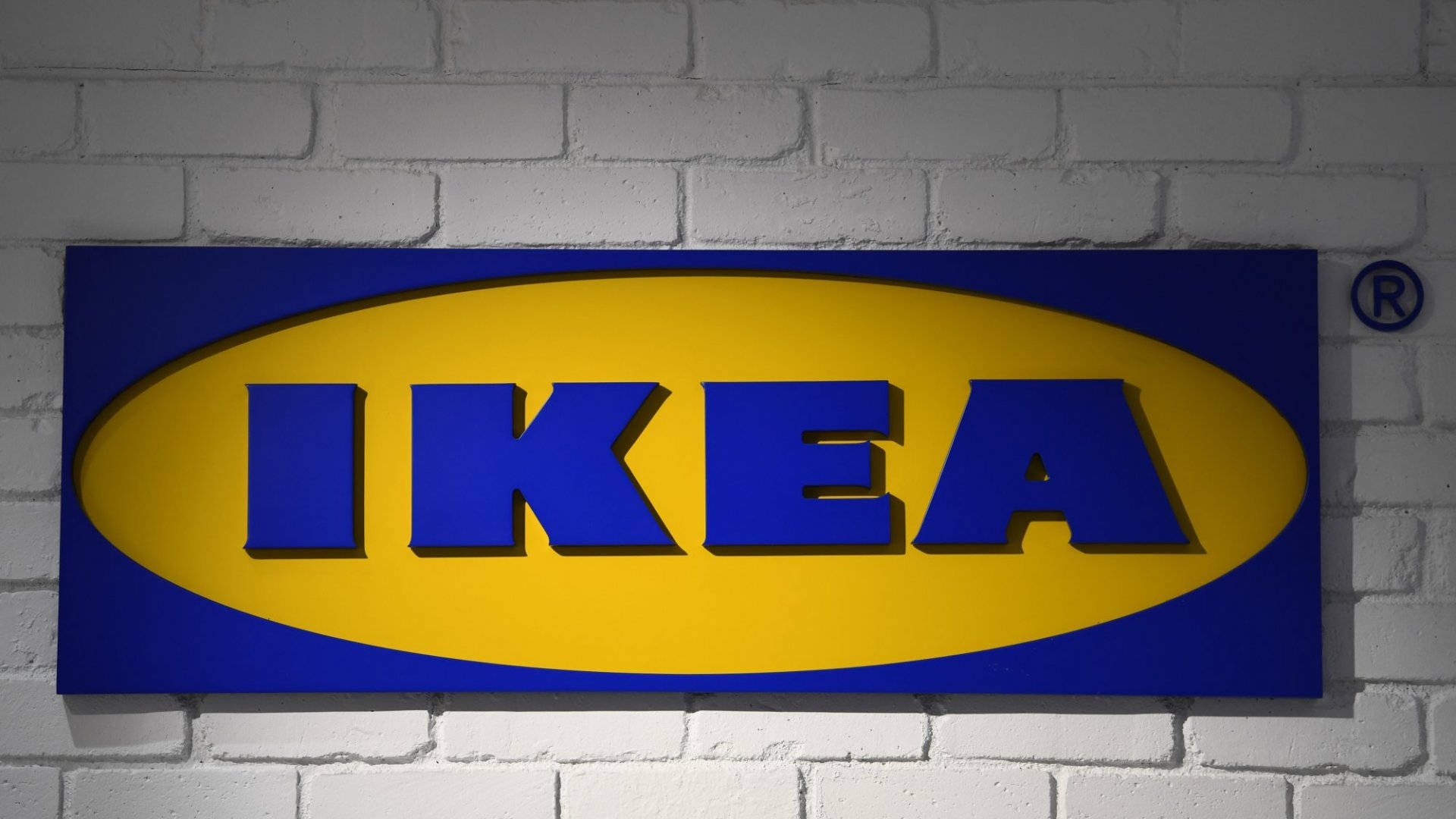 Brick Wall 桌布 壁紙 — 一個大膽的藍色和黃色 IKEA 標誌牌安裝在白色磚牆上，在聚焦照明下。