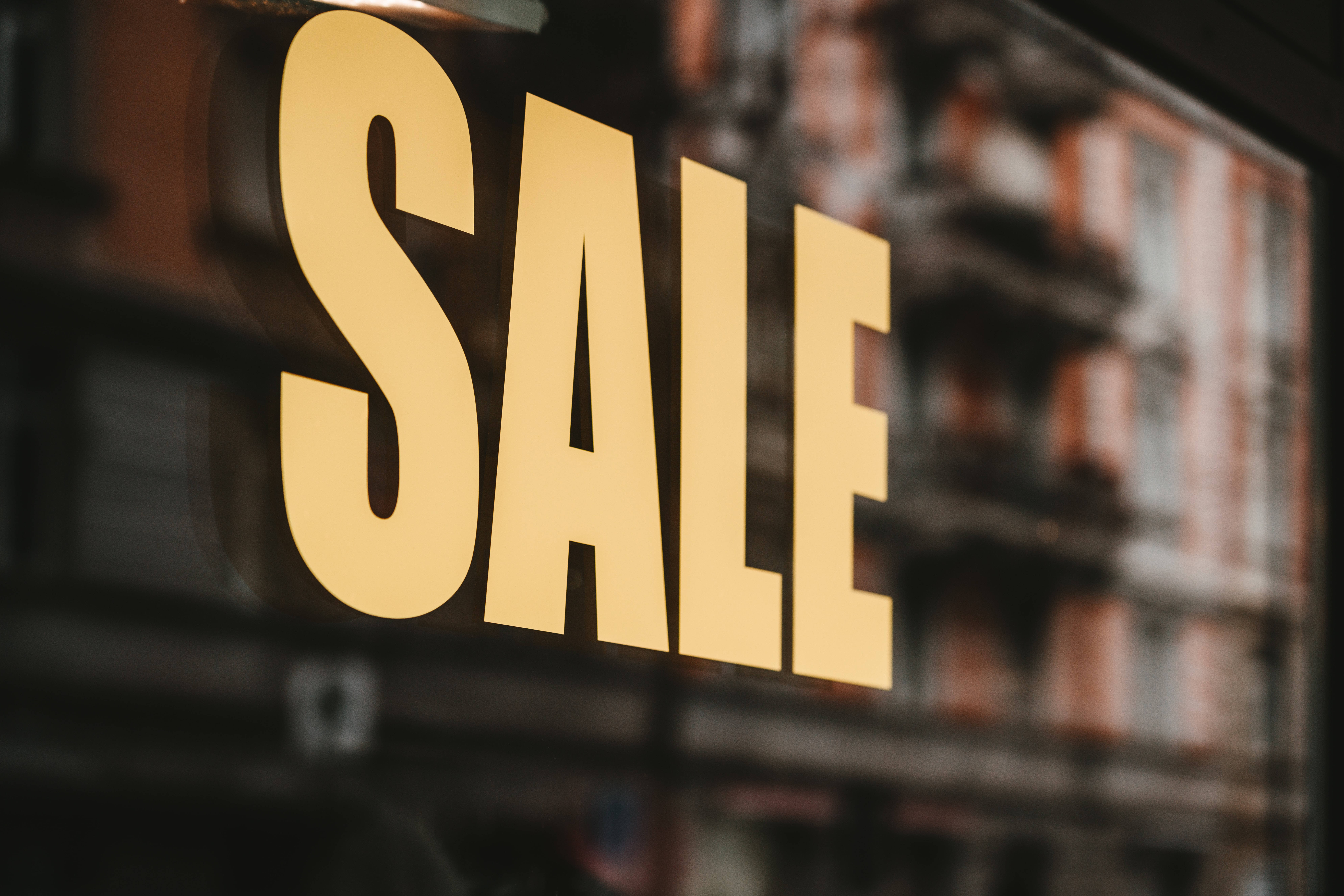 Shopping 桌布 壁紙 — 一個大膽的金色SALE標誌透過商店櫥窗發光，反射出模糊的磚砌建築外牆。