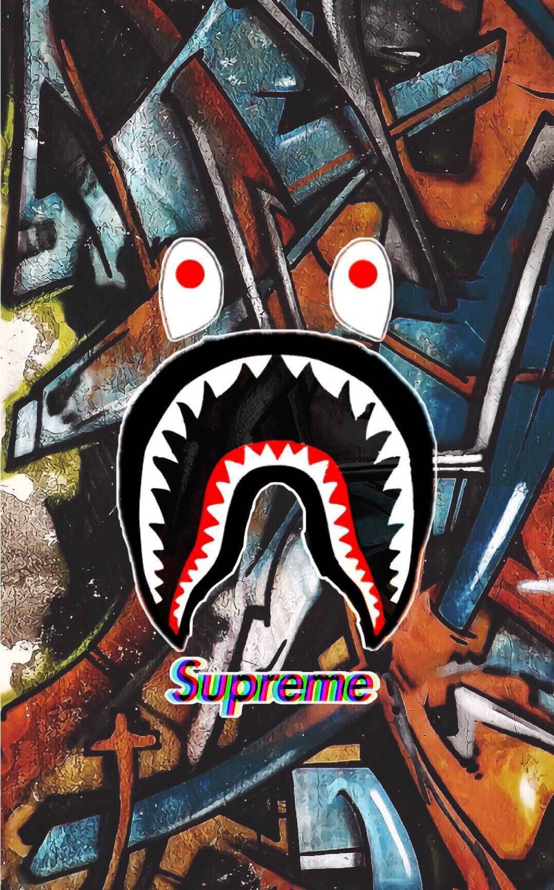 bape logo 桌布 壁紙 — 一個大膽的鯊魚頭標誌，帶有紅色眼睛和牙齒，置於混亂的塗鴉牆上，搭配鮮豔的抽象色彩。