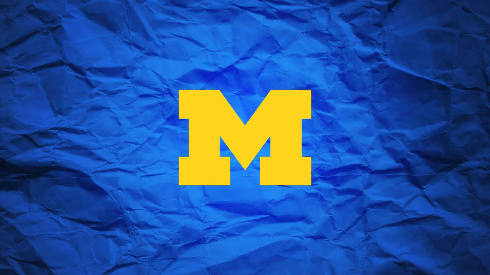 Michigan Football 桌布 壁紙 — 一個大膽的黃色「M」標誌在帶有紋理的藍色皺紙背景上脫穎而出。
