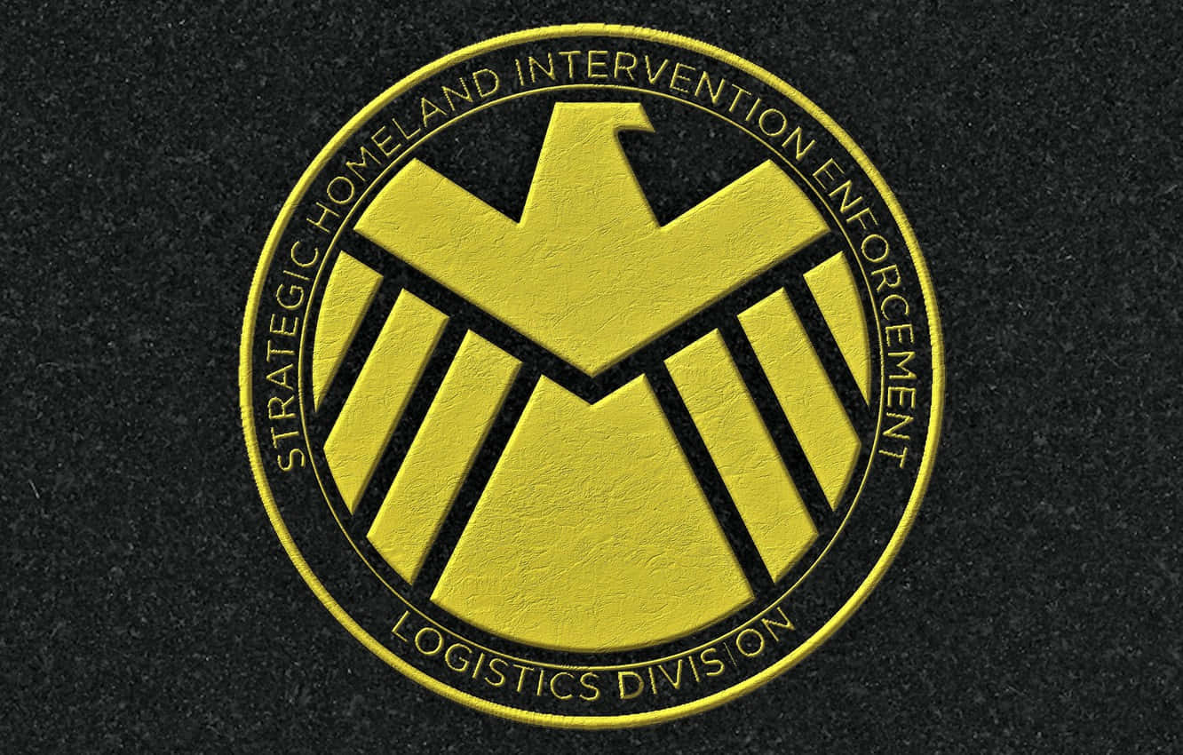 Marvel Logo 桌布 壁紙 — 一個大膽的黃色SHIELD Logistics Division徽章，帶有鷹圖案，位於紋理黑色布料背景上。