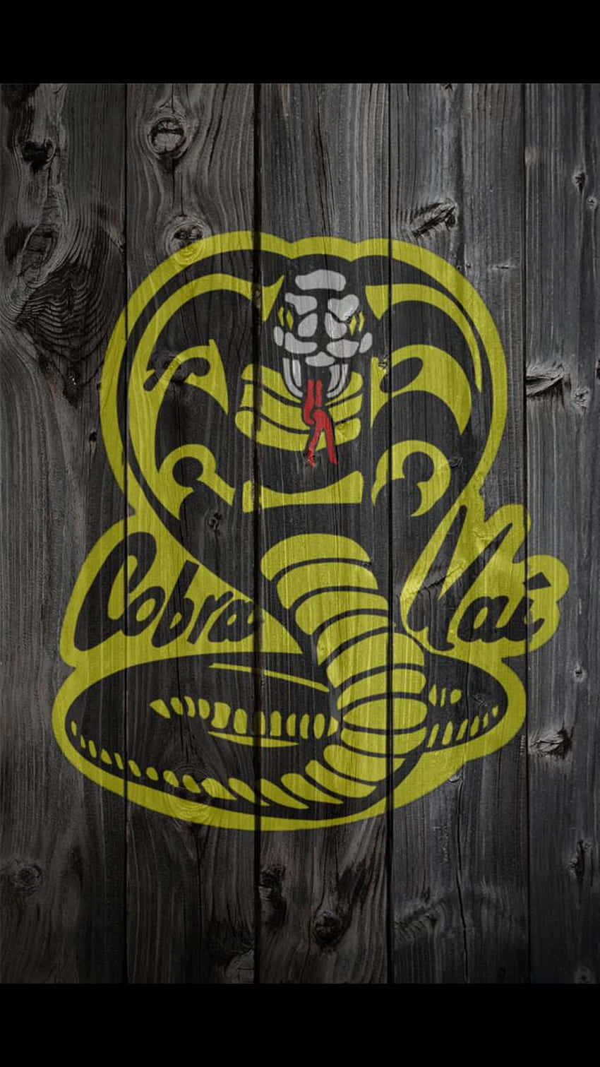眼鏡蛇道館 桌布 壁紙 — 一個大膽的黃色和黑色 Cobra Kai 標誌，塗在風化的深色木板上，可見木紋和節疤。