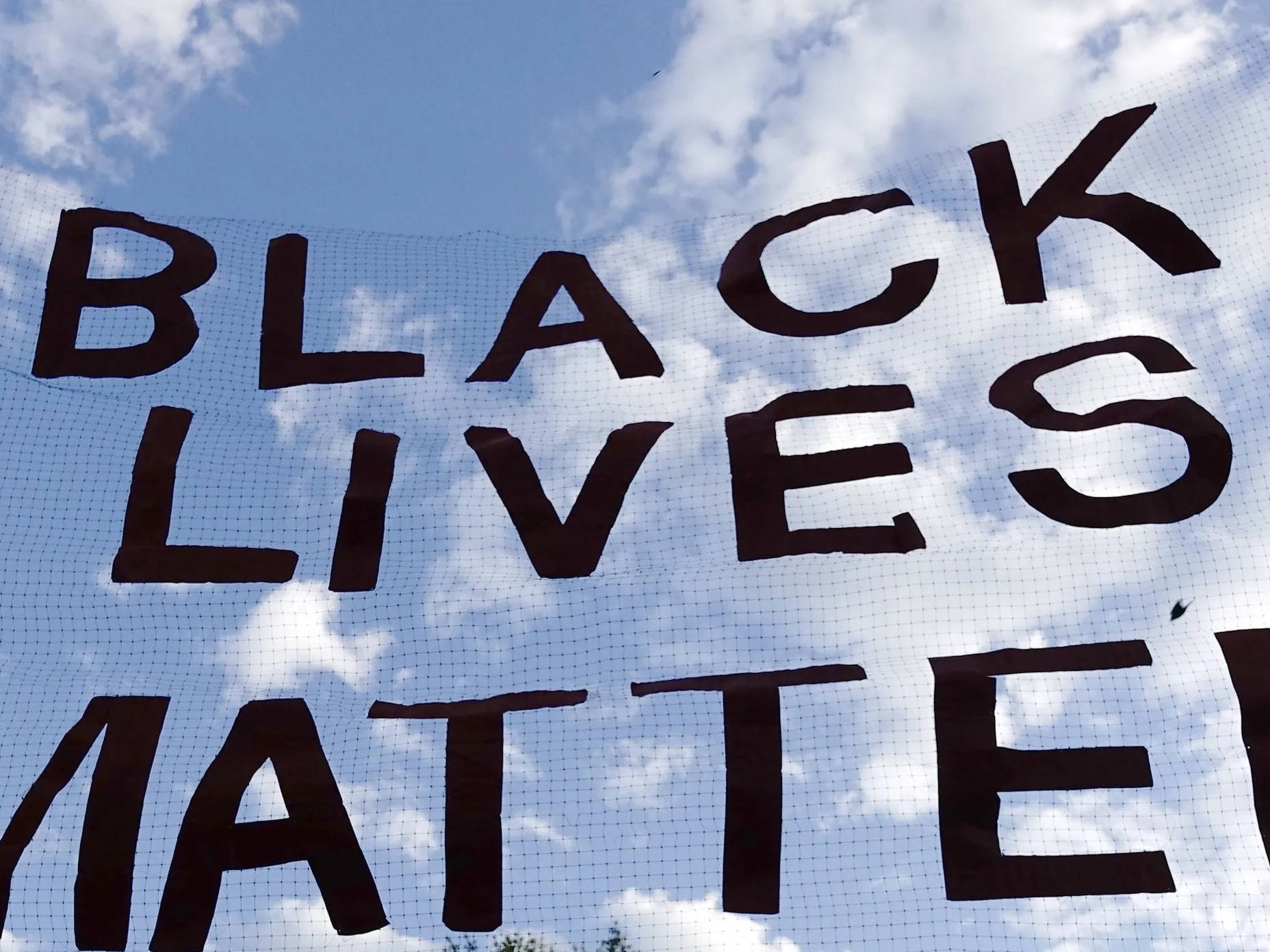 美國 桌布 壁紙 — 一個大膽的黑色「BLACK LIVES MATTER」抗議標語牌掛在明亮的藍天和白雲之間。