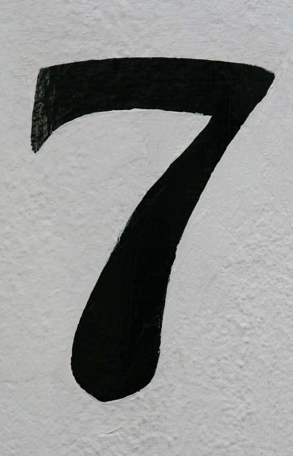 Number 7 桌布 壁紙 — 一個大膽的黑色數字七，塗在粗糙的白色紋理牆上，可見筆觸。