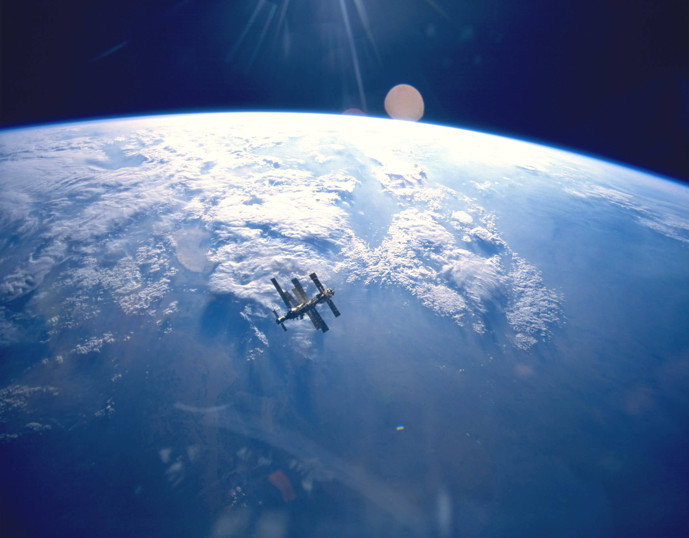 NASA 動態圖片 桌布 壁紙 — 一個太空站繞地球運行，展示出旋轉的雲層和藍色海洋，背景是太空的漆黑，陽光穿透其中。