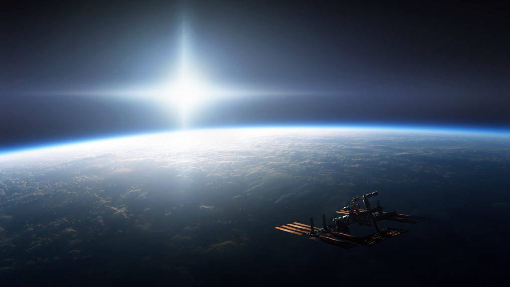 太空電腦 桌布 壁紙 — 一個太空站繞著地球運行，太陽在行星彎曲的地平線上方明亮地照耀。