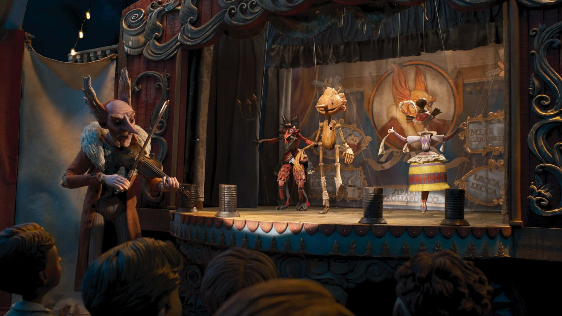 Guillermo Del Toro's Pinocchio 桌布 壁紙 — 一個奇特的木偶劇舞台，帶有華麗的木製裝飾，三個木偶在溫暖的舞台燈光下表演。