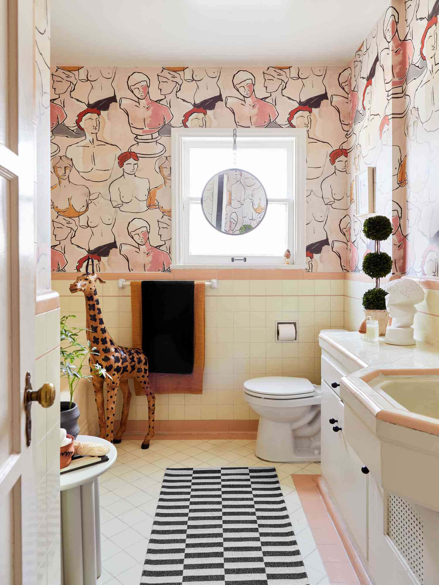 Bathroom Decor 桌布 壁紙 — 一個奇特的浴室，粉紅色和米色的牆壁上佈滿了插圖半身像、一隻長頸鹿雕像和一張黑白條紋地毯。