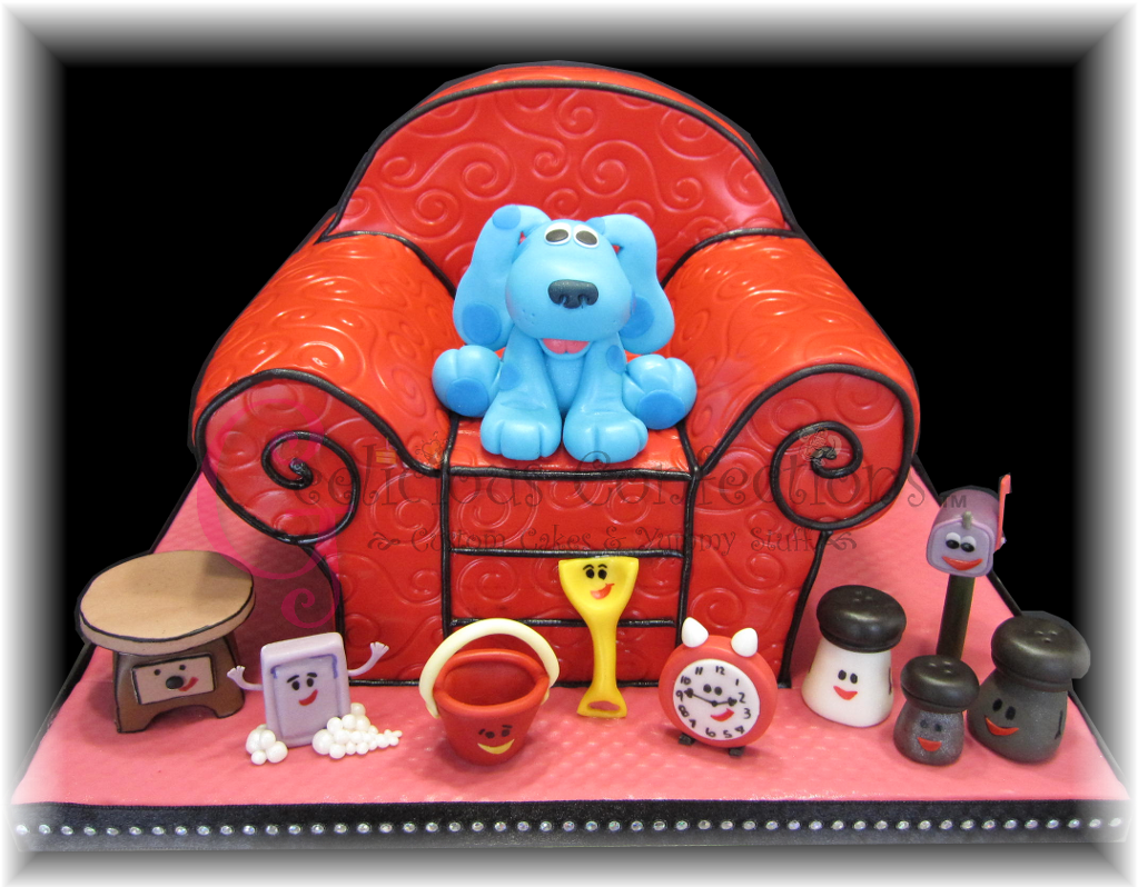 Blues Clues 桌布 壁紙 — 一個奇特的蛋糕，形狀像紅色扶手椅，上面坐著一隻藍色小狗雕像，周圍是微笑的玩具狀物體，放在粉紅色底座上。
