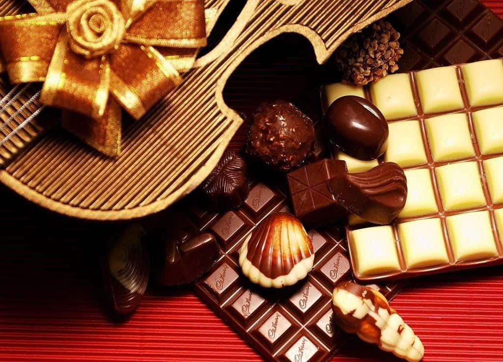 Chocolate 桌布 壁紙 — 一個奢華的巧克力組合，包括黑巧克力、牛奶巧克力和白巧克力，以金色蝴蝶結裝飾在紅色紋理表面上。