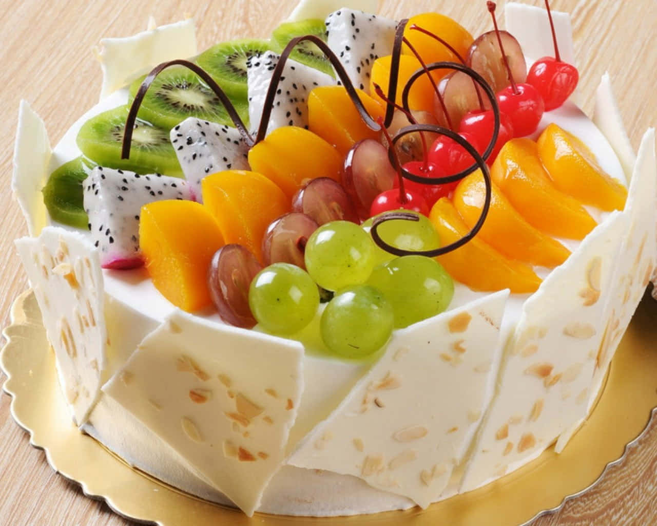Delightful 桌布 壁紙 — 一個奢華的水果頂層蛋糕，飾以奇異果、火龍果、葡萄、櫻桃和柳橙片，放在金色盤子上。