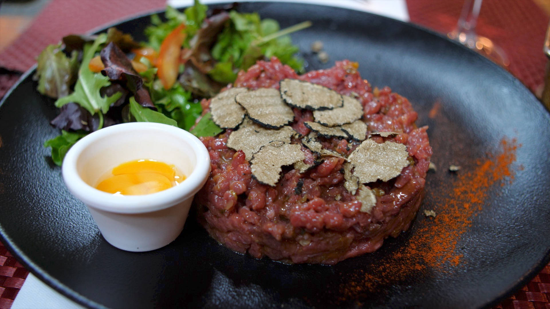 meat 桌布 壁紙 — 一個奢華的牛肉他他，上面鋪有黑松露片，旁邊配上生蛋黃，放在深色盤子上。