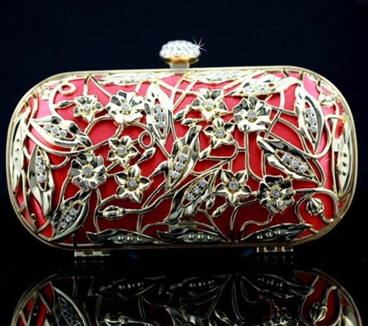 purse 桌布 壁紙 — 一個奢華的紅色手拿包，飾有金色花卉鏤空圖案和閃亮水鑽，放置在反光的黑色表面上。
