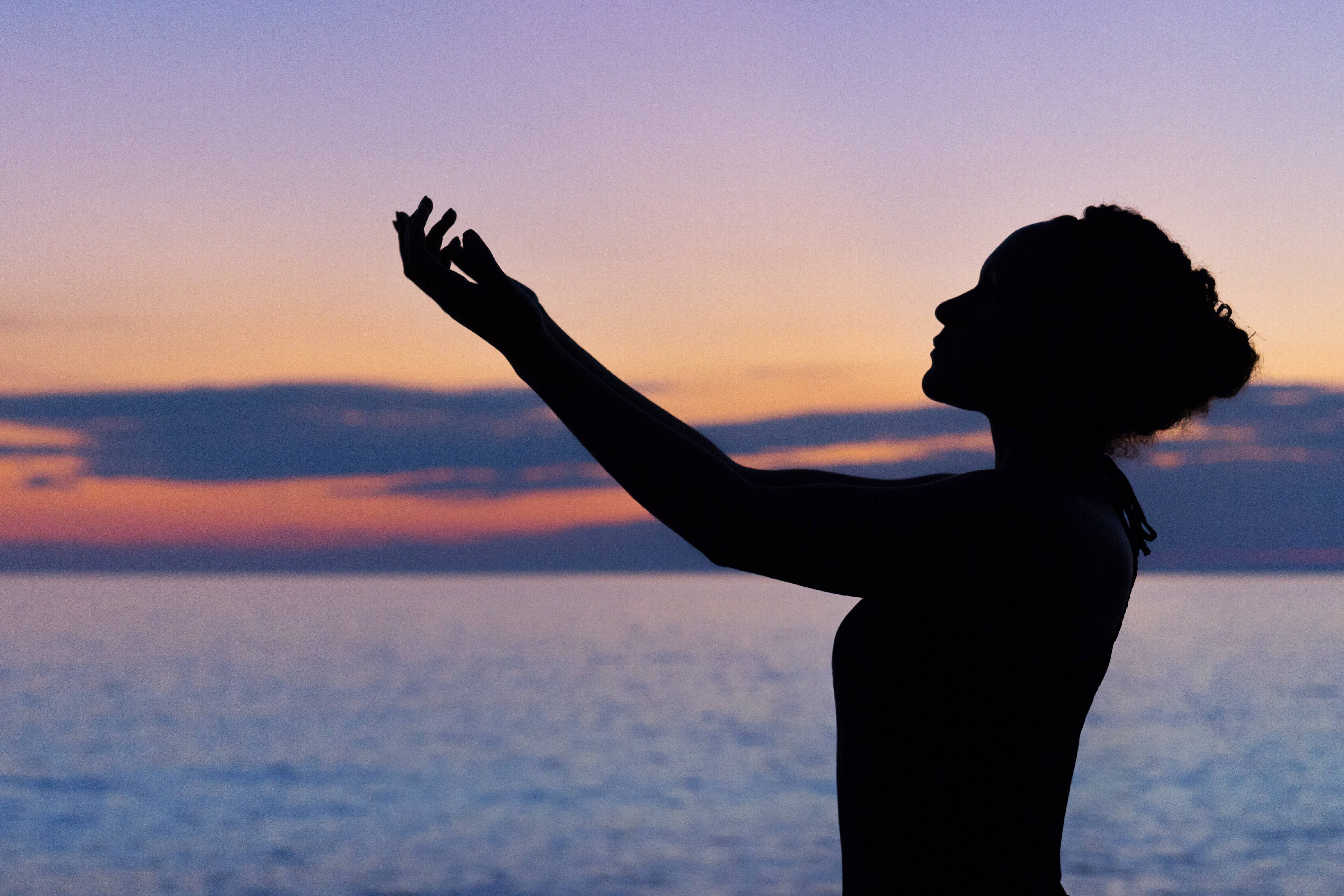 Praying 桌布 壁紙 — 一個女人在平靜的海面上伸手觸及充滿活力的日落的剪影。
