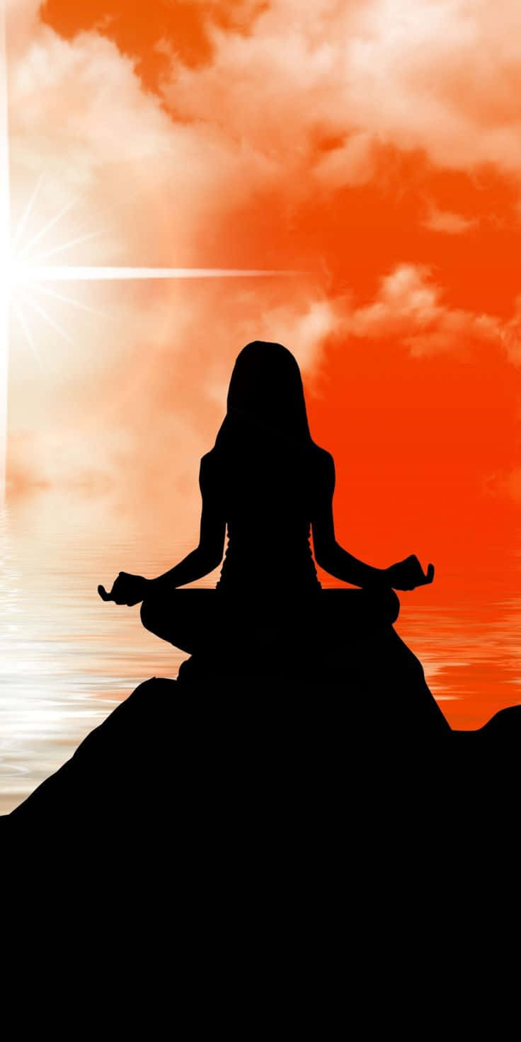 Spiritual Meditation 桌布 壁紙 — 一個女人在日落時分盤腿坐在岩石上冥想的剪影，天空是充滿活力的橙色，下面是平靜的水面。