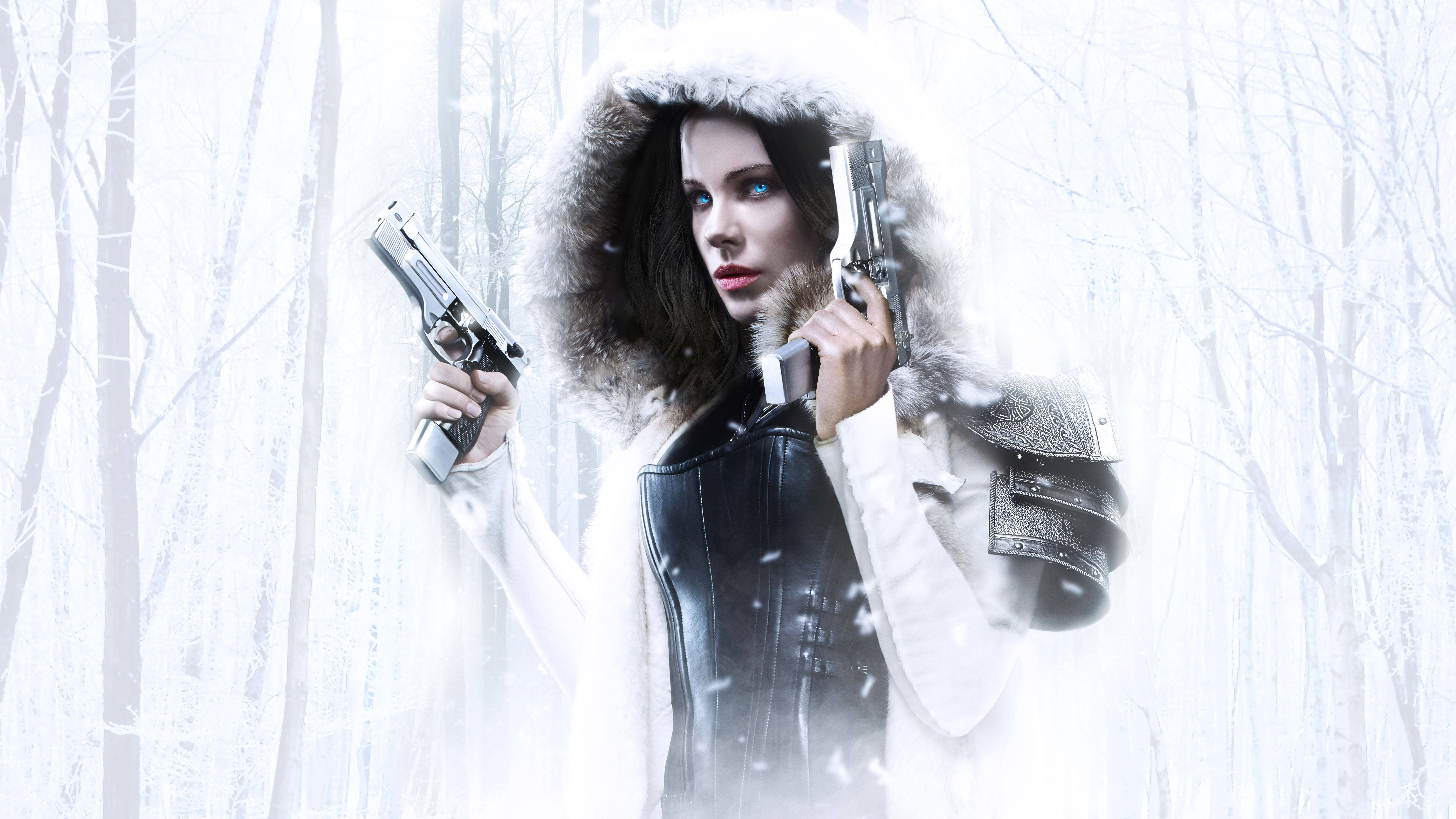 Kate Beckinsale 桌布 壁紙 — 一個女人在雪地森林中，戴著毛皮襯裡的兜帽，手持兩把手槍，雪花在她周圍飄舞。