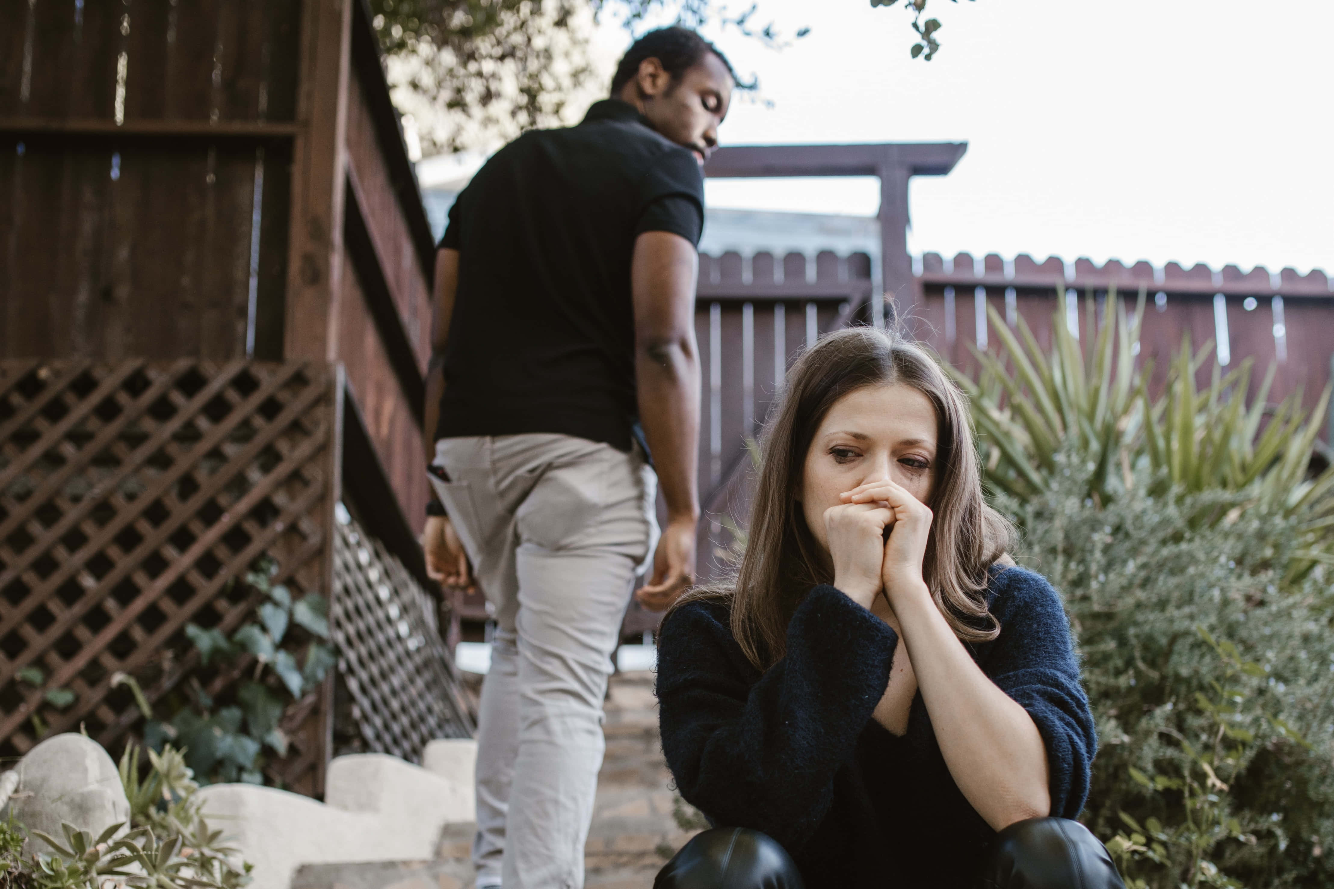 Sad Couple 桌布 壁紙 — 一個女人坐在花園裡，看起來很苦惱，一個男人穿過木柵欄走開。