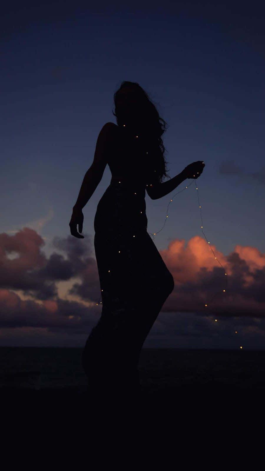 Silhouette 桌布 壁紙 — 一個女人拿著燈串的剪影，背景是帶有粉紅色和紫色雲彩的暮色天空。