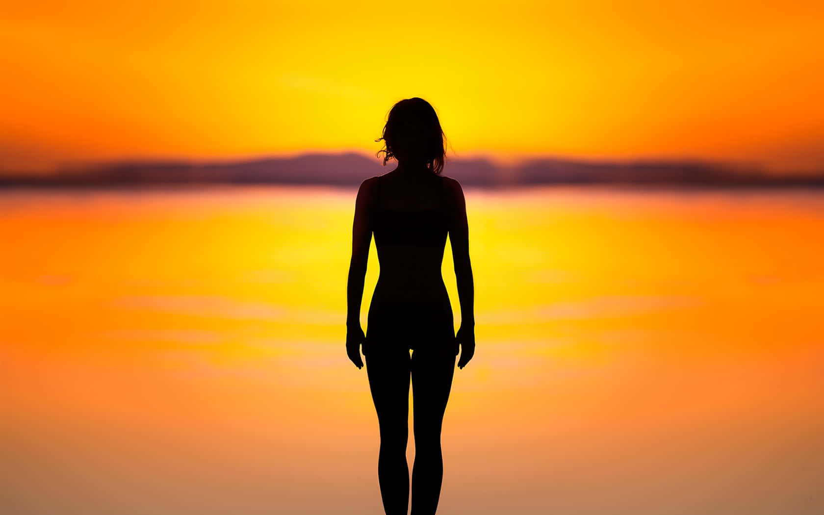 Silhouette 桌布 壁紙 — 一個女人獨自站在日落時分的剪影，面向水面上發光的橙色地平線。