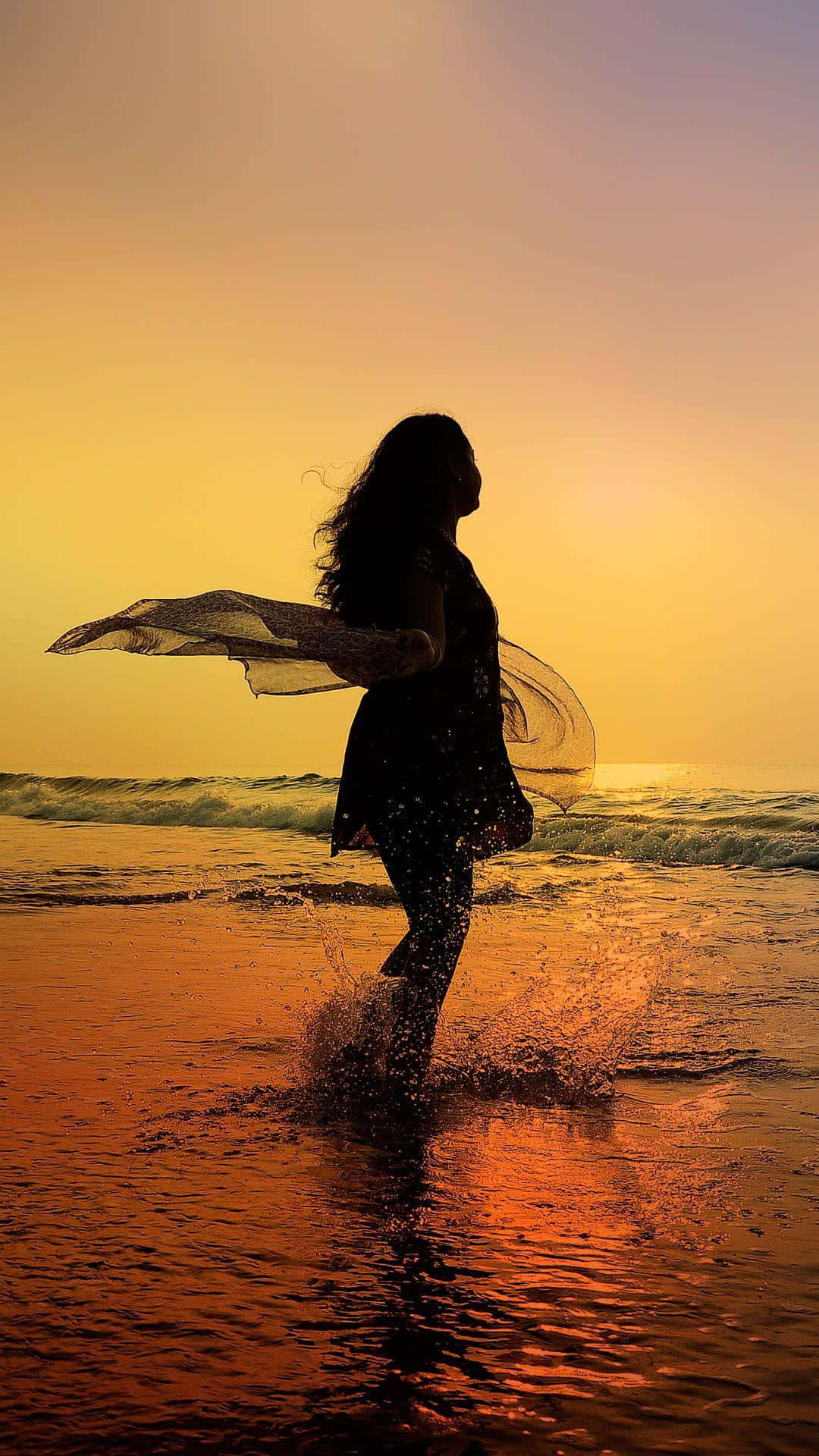 Sunset Silhouette 桌布 壁紙 — 一個女人的剪影在淺海水中跳舞，金色的夕陽光芒以溫暖的色調沐浴著海灘。