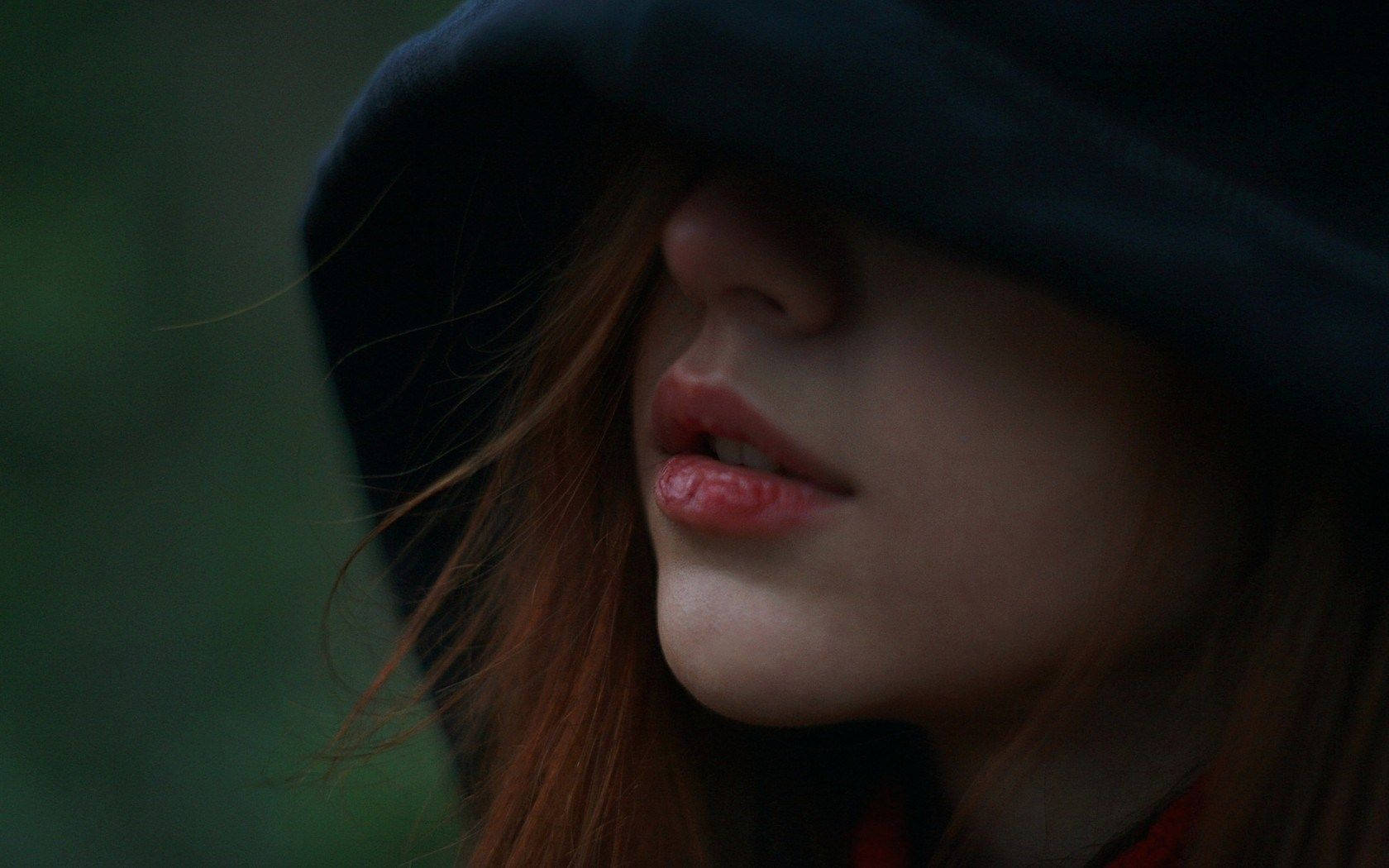 Face 桌布 壁紙 — 一個女人的嘴唇和下巴在深色兜帽下露出，搭配柔軟紅髮，背景是模糊的綠色。