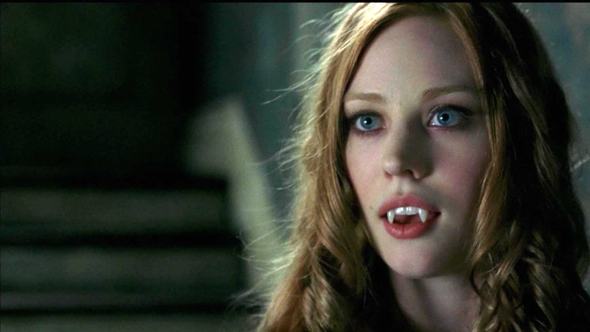 True Blood 桌布 壁紙 — 一個女人的特寫，她有藍色眼睛和獠牙，在昏暗的環境中。