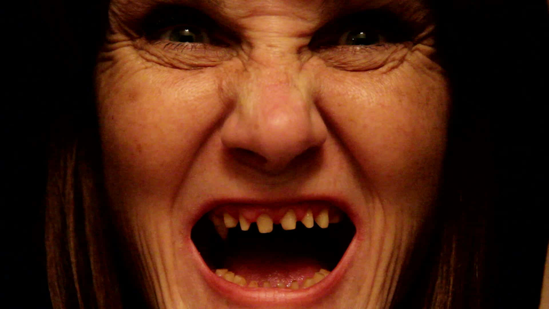 Scary Face 桌布 壁紙 — 一個女人的臉在尖叫中扭曲，露出牙齒，背景是黑暗的。