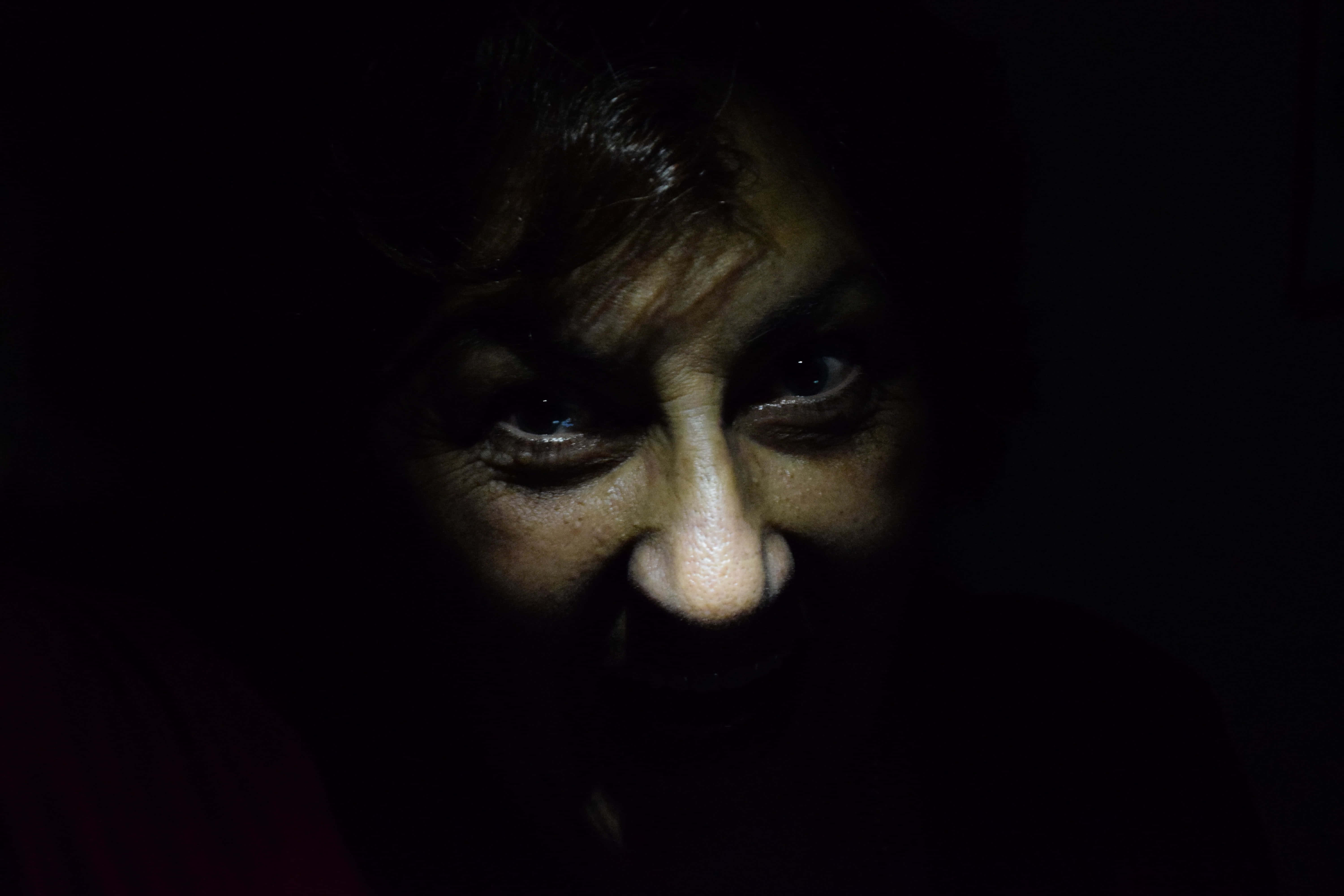 Dark Fear 桌布 壁紙 — 一個女人的臉在黑暗中戲劇性地被照亮，她強烈的眼睛和皺起的眉頭傳達出深刻的情感。