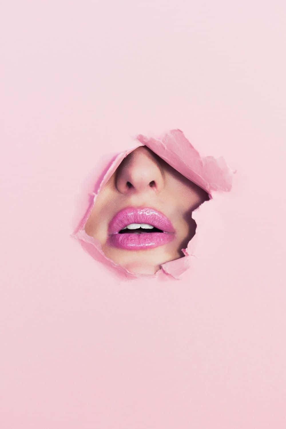 Cute Makeup 桌布 壁紙 — 一個女人的臉從撕破的粉紅色紙張中窺視，露出光澤的嘴唇和鼻子，背景是柔和的粉紅色。