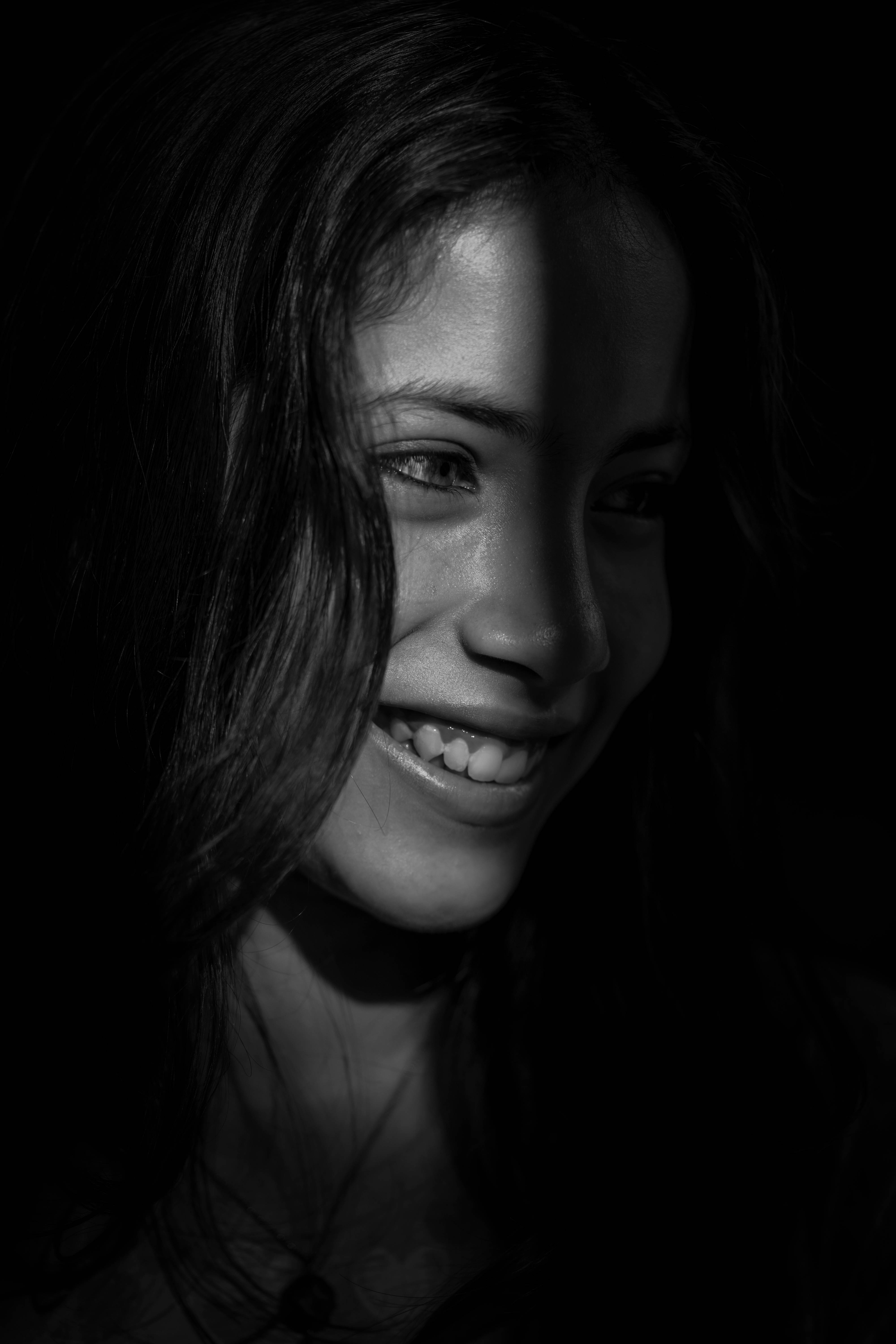 Smile 桌布 壁紙 — 一個女人的臉被戲劇性的明暗對比照明照亮，背景為黑色，捕捉到一個快樂的微笑。